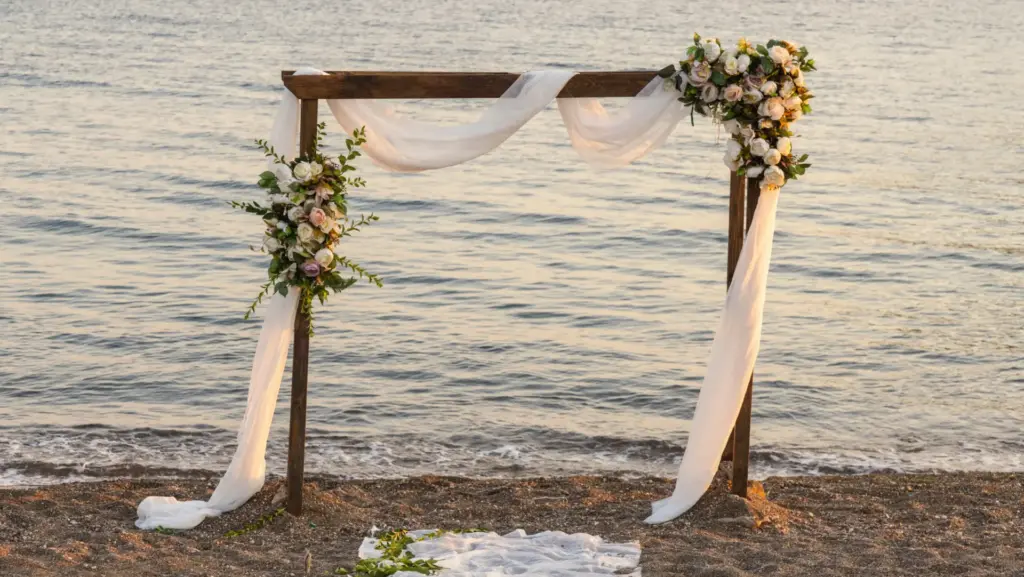 schöner Holzrahmen mit Blumen und einem weißen Tuch am Strand aufgebaut